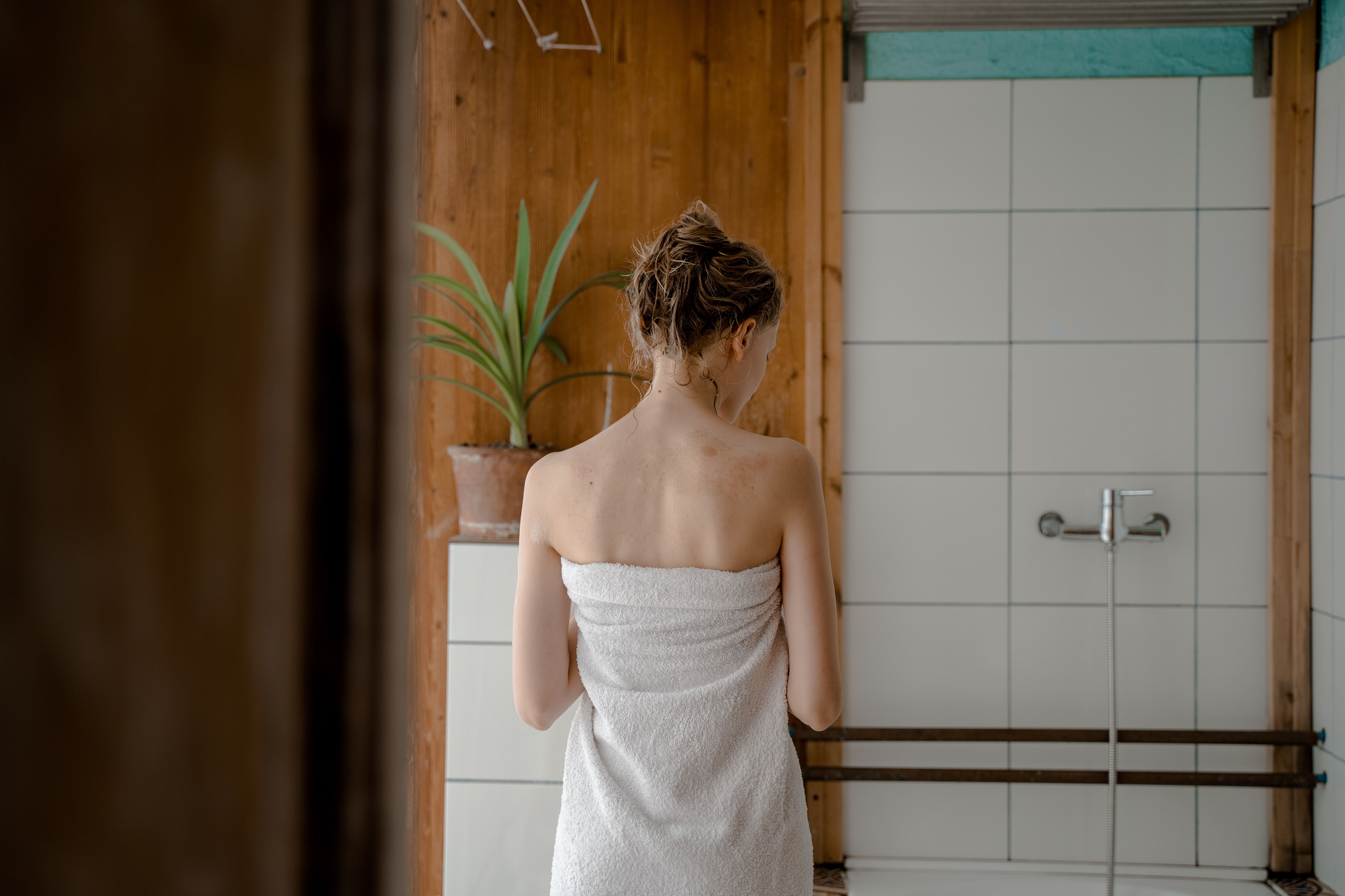Kobieta owinięta ręcznikiem stoi w łazience po kąpieli. | Źródło: Pexels