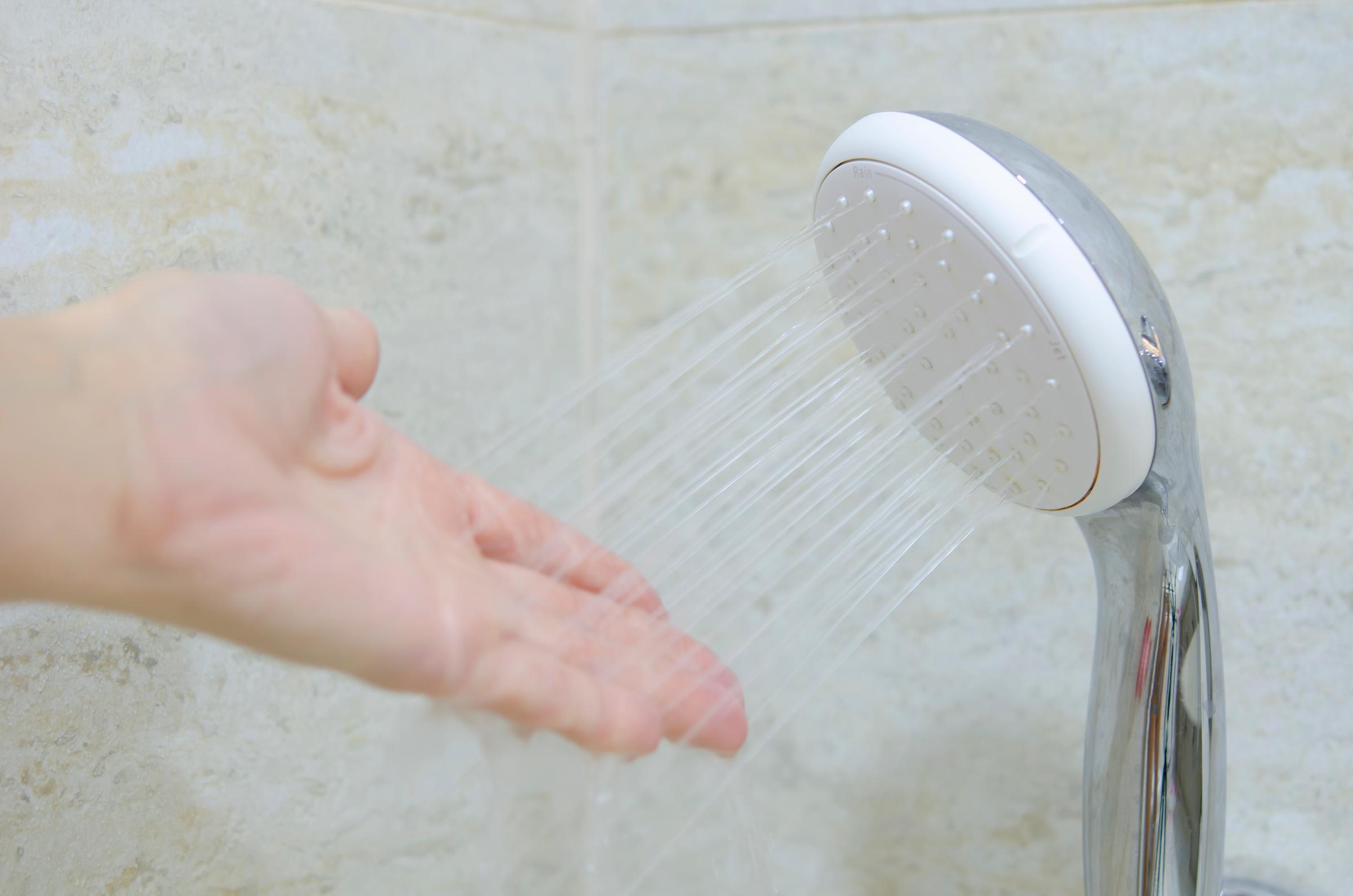 Dłoń czująca wodę wypływającą z wylewki prysznica | Źródło: Shutterstock