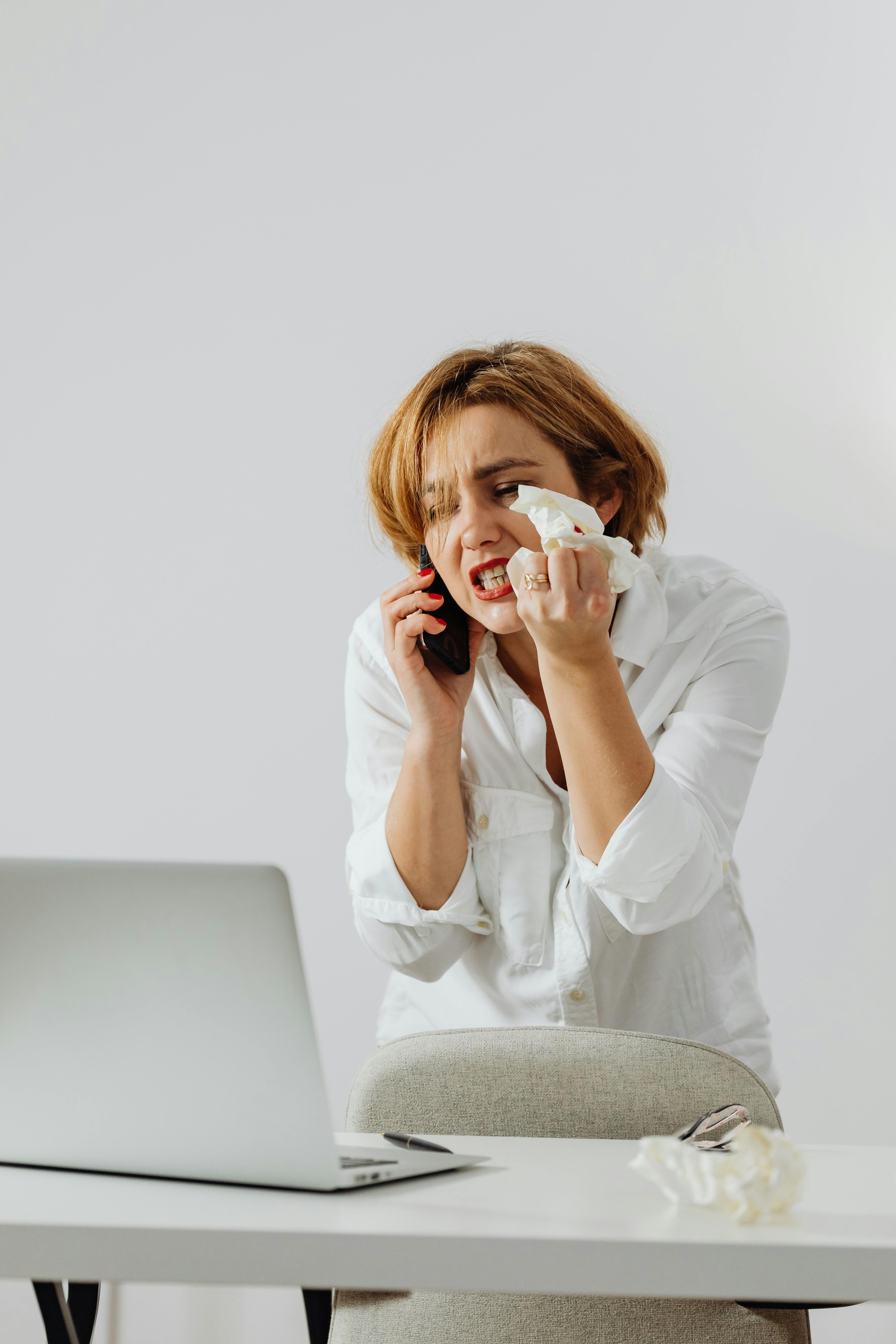 Kobieta krzyczy przez telefon, siedząc przed laptopem | Źródło: Pexels